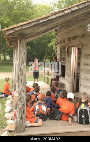 Austin, Texas USA, May 2006: Third grade students listen on porch of one-room schoolhouse while fellow student reads from old textbook during school field trip to restored 19th-century farm.  ©Bob Daemmrich Stock Photo