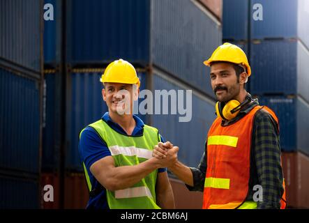 Two Industrial workers or engineers join hands together for better work in logistics business at container yard. Stock Photo