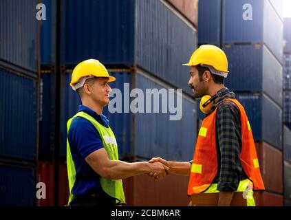 Two Industrial workers or engineers join hands together for better work in logistics business at container yard. Stock Photo