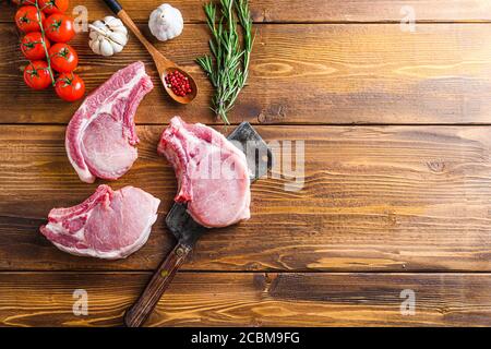 Raw pork meat chopes with herbs and spices with meat american cleaver on wooden background space for text. Stock Photo