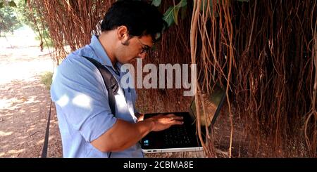 DISTRICT KATNI, INDIA - OCTOBER 23, 2019: An indian corporate male executive working on laptop around natural tree environment background. Stock Photo