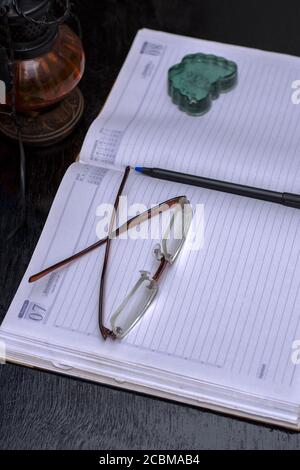 An empty office notebook with pen eye glasses with a lamp shade in background Stock Photo
