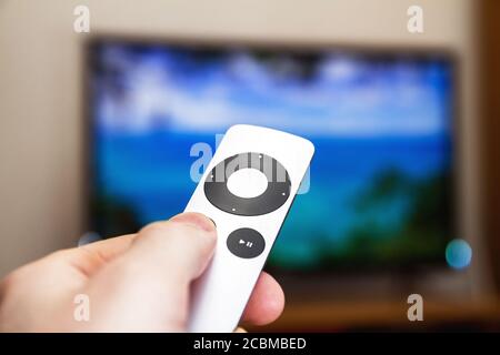 Man presses a button on the modern grey steel remote controll on the background of the TV turned off. A man controls a TV Stock Photo