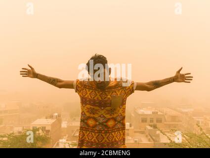 youth/juvenile opening up arms with a serious expression in sandstorm Stock Photo