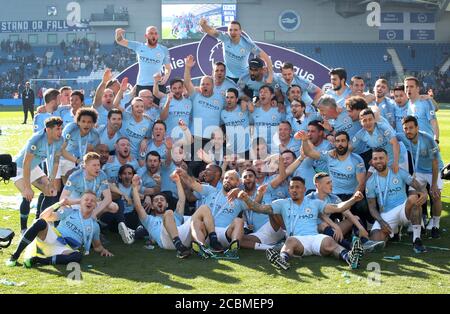 Manchester City manager Pep Guardiola (centre) celebrates winning the Premier League Trophy with his players, backroom and coaching staff during the Premier League match at the AMEX Stadium, Brighton. Stock Photo