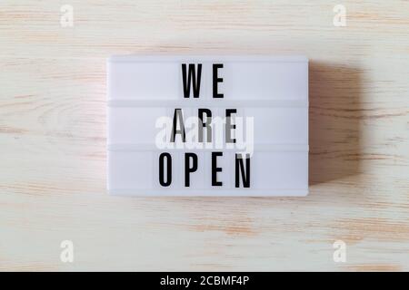 Signboard WE ARE OPEN of lightbox on wood background. Open sign hanging on vintage wooden wall. Opening sign of cafe, bar, or restaurant. Business ope Stock Photo