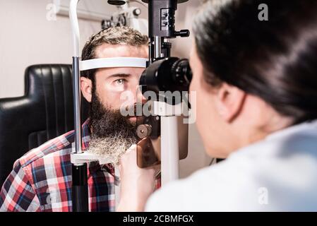 Woman examines the sight of a bearded man in optical center using a slit lamp