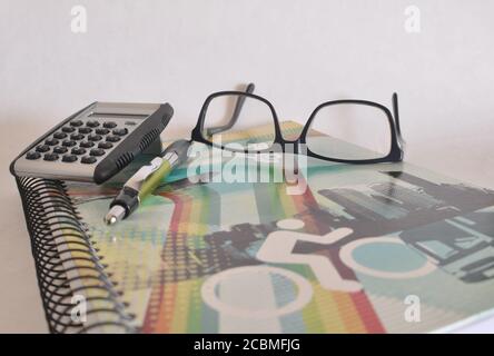 Writing notebook with colored cover, glasses, pen and non-digital calculator on white background, concept photo, back to school, Brazil, South America Stock Photo