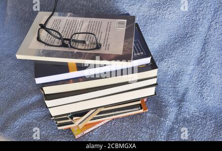 Stack of books for study, various topics with reading glasses on blue background, Brazil, South America Stock Photo