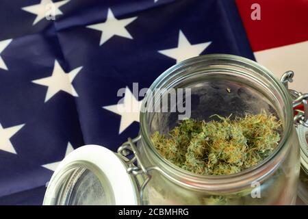 Big Glass Jar of Weed Buds with USA national flag background. Cannabis close-up with copy space Stock Photo