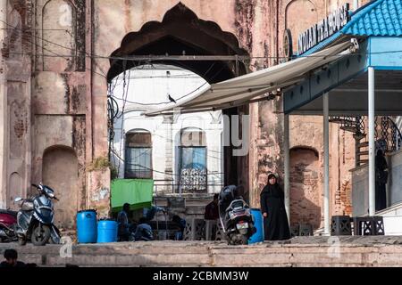 Bhopal, Madhya Pradesh,India - March 2019: An Indian woman wearing a black burkha walks in front of the grand arched gateway of the ancient Shaukat Ma Stock Photo