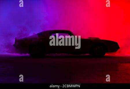 Silhouette of an old fashion muscle car on a red and blue background with some fog like doing burnout. Stock Photo