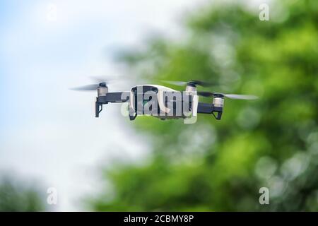 Small drone in flight against defocused foliage. Selective focus on the drone Stock Photo