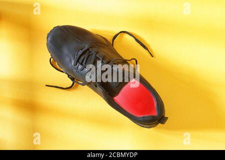 Single black boot with red illumination inside on yellow background top view. Abstract walking and footwear theme image Stock Photo