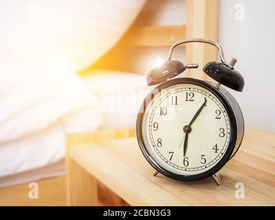 Alarm clock , wake-up time concept : Retro alarm clock with five minutes past six o'clock in the morning on wooden bed side table with white bed sheet Stock Photo