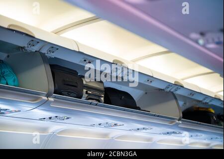 Carry-on luggage in overhead shelf in airplane cabin Stock Photo