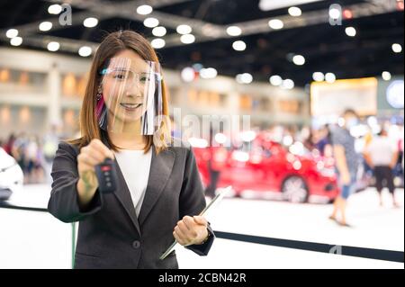 Asian car seller wearing face mask presents car and passing new car key to customer after purchased while coronavirus pandemic Stock Photo