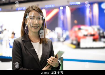 Asian female car seller wearing face mask presents detail of vehicle while conoravirus pandemic Stock Photo