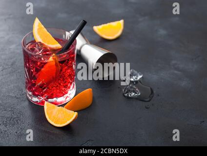 Negroni cocktail in crystal glass with orange slice and fresh raw oranges with jigger and ice cubes on black background. Top view Stock Photo