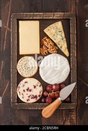 Selection of various cheese in wooden box with grapes and nuts on wooden table background. Blue Stilton, Red Leicester and Brie Cheese and knife. Stock Photo