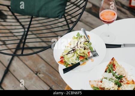 Homemade pizza and aperol drink on modern white table on terrace, dinner for two. Delicious pizza and cocktails for home or cafe celebration. Summer v Stock Photo