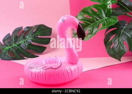 Inflatable pink mini flamingo and tropical leaf monstera on pink background. Summer background. Creative summer beach concept. Flamingo Trend Inflatable Toy. Stock Photo