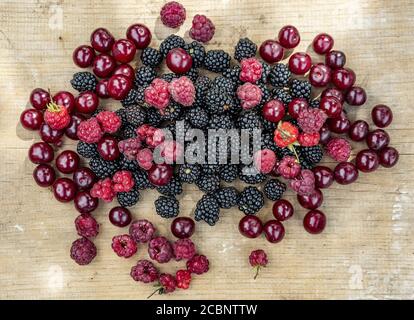 Summer gifts, ripe blackberries, red cherries and raspberries lie on a wooden table Stock Photo