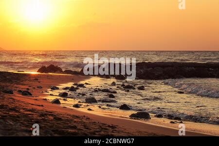 Sunset on wild beach, sun shines on wet stones in sand Stock Photo