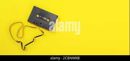 Overhead shot - magnetic audio cassette with some tape out, on yellow board, wide banner space for text on right side. Stock Photo