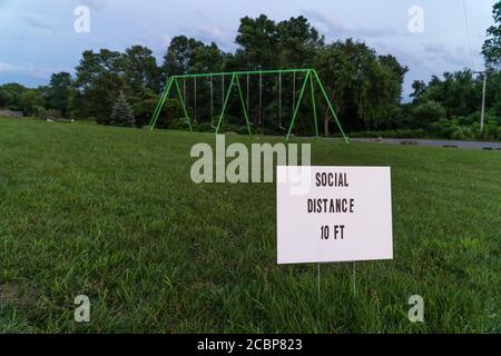 Sign stating social distance 10 feet at empty playground with swingset in background Stock Photo