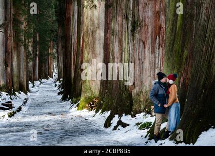 couple posing with Giant Cedar Trees in natural forest with snow and fog in winter season, Togakushi Jinja, Nagano, Japan. Tourist in travel trip. Stock Photo