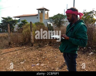 DISTRICT KATNI, INDIA - JANUARY 01, 2020: An indian village local man operating laptop at open area industrial background. Stock Photo