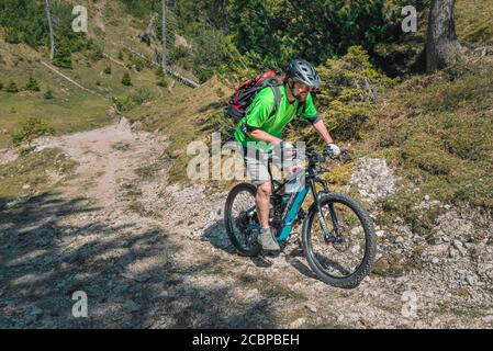 Mountain biker rides with eMTB on a cart track in the mountain forest downhill, Rofangebirge, Steinberg am Rofan, Tyrol, Austria Stock Photo