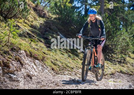 Female mountain biker rides with eMTB on a cart track uphill in the mountain forest, Rofan Mountains, Steinberg am Rofan, Tyrol, Austria Stock Photo