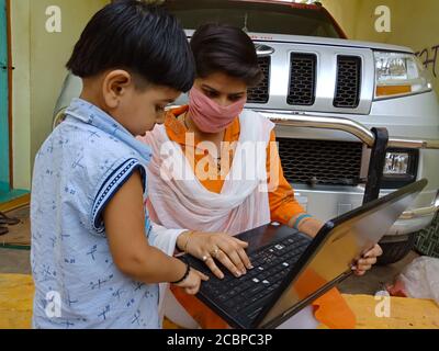 DISTRICT KATNI, INDIA - MAY 16, 2020: An indian girl teaching little boy about laptop technology at home also wearing face mask for corona virus. Stock Photo