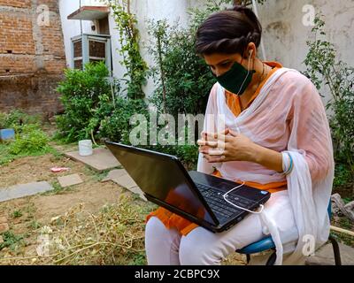 DISTRICT KATNI, INDIA - MAY 16, 2020: An indian girl wearing face mask for corona virus protection during laptop video Conferencing at open area, work Stock Photo