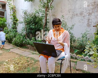 DISTRICT KATNI, INDIA - MAY 16, 2020: An indian corporate girl doing video webinar on laptop while work from home at garden. Stock Photo