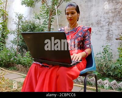 DISTRICT KATNI, INDIA - MAY 16, 2020: An indian village traditional female working on laptop wearing sari at garden. Stock Photo