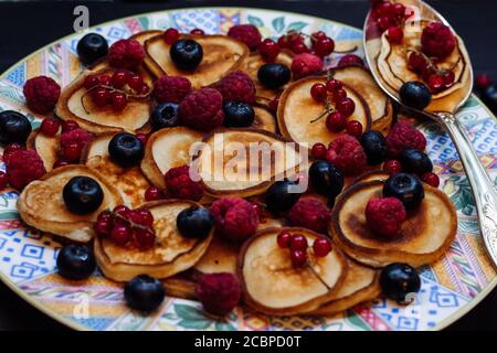 Mini pancakes with fresh summer berries on white plate with cute patterns and silver spoon in rustic style. Stock Photo