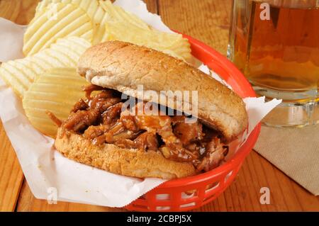 A pulled pork or beef sandwich in a basket with potato chips and beer Stock Photo