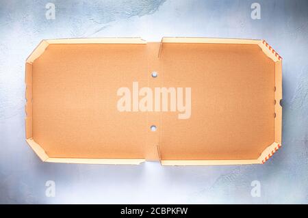 Whole new clean brown opened empty pizza box made of paperboard on blue stone textured background with shadows. Horizontal orientation. Large copy spa Stock Photo