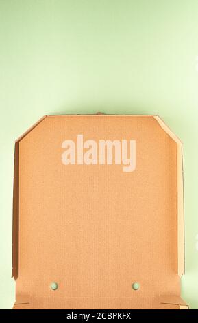 Part of new clean brown opened empty pizza box made of paperboard on light green or mint paper background with shadows. Vertical orientation. Large co Stock Photo
