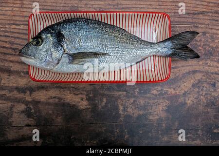 Raw sea bream on red and white striped ceramic plate on wooden table Stock Photo