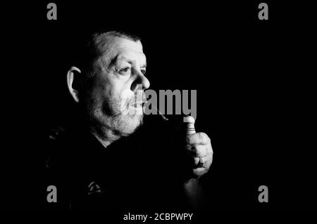 Nice Black and white dramatic portrait of caucasian senior smoking tobacco pipe in darkness Stock Photo