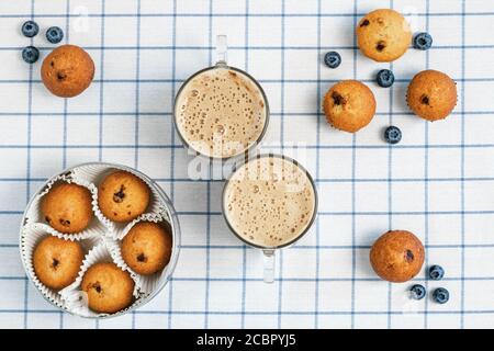 Two cups of frothy coffee and blueberry muffins on a checkered tablecloth. Breakfast concept. Flat Lay design. Food background, wallpaper Stock Photo