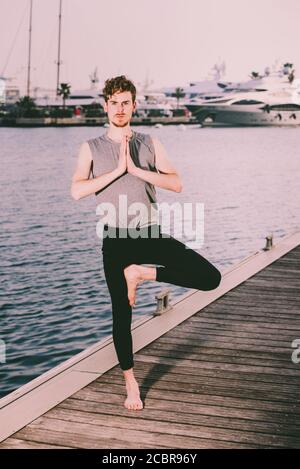Young redhead practicing yoga, Vriksasana tree posture, to concentrate and help him with his mindfullness Stock Photo