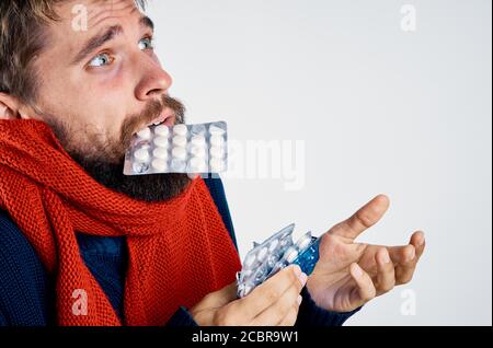 A man with pills in his teeth gestures with his hands health problems warm clothes red scarf Stock Photo