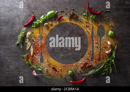 Spices and herbs scattered on the table forming the silhouette of cutlery and a plate. Stock Photo