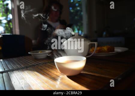A black tea service set, with steaming porcelain cup of tea and tea cattle. Stock Photo