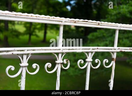 Old aged railing with retro and vintage spiral decoration. Green grass and trees in the blurred background Stock Photo